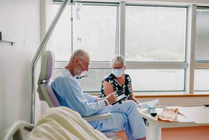 Patient assis sur un fauteuil d'hôpital consultant son téléphone avec sa femme assise à côté de lui