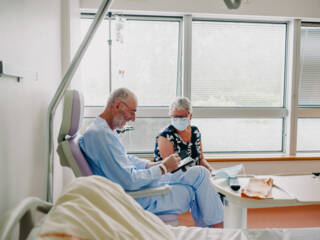 Patient assis sur un fauteuil d'hôpital consultant son téléphone avec sa femme assise à côté de lui